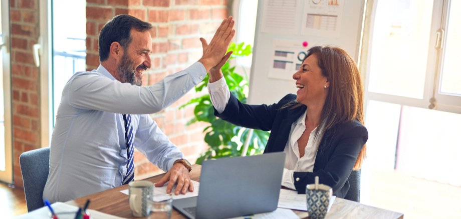 2 Menschen am Schreibtisch geben sich high five