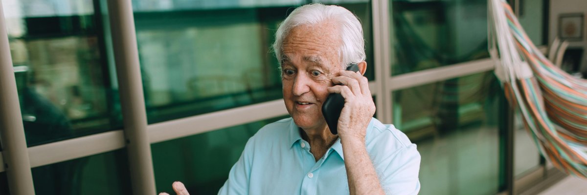 Älterer Mann mit Handy am Ohr und Laptop